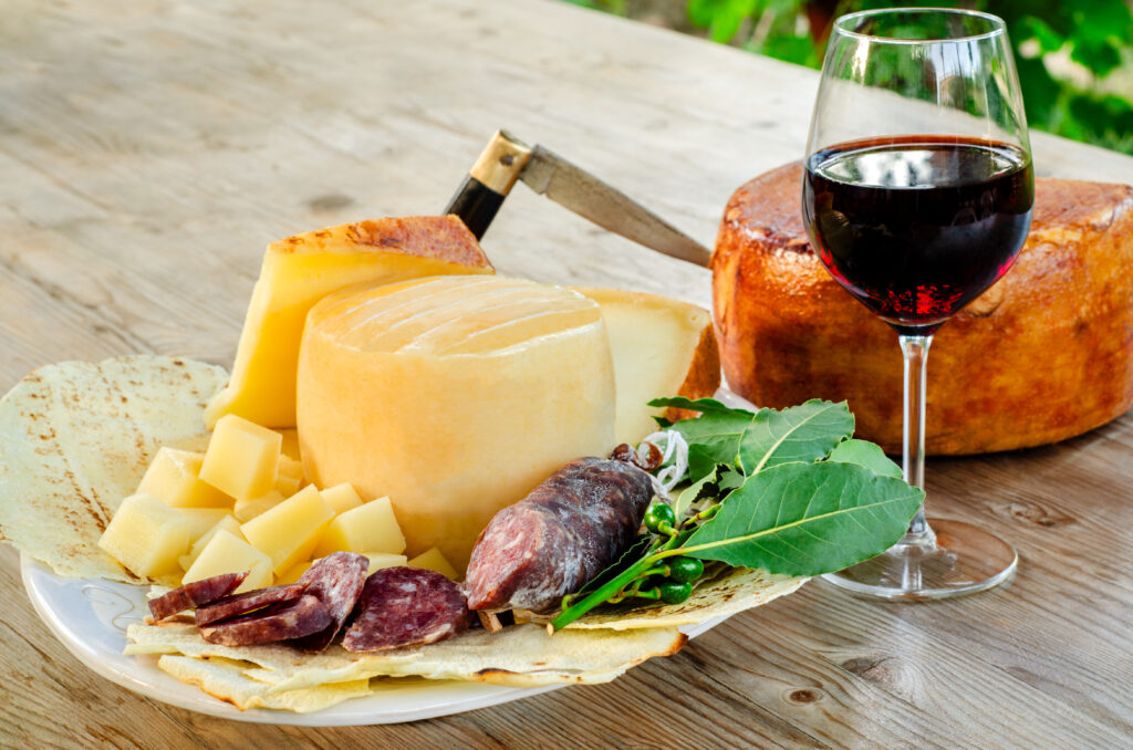 Home vassoio con pecorino sardo e salsiccia secca di maiale, accompagnati da un calice di vino cannonau rosso, gastronomia sarda, cibo italiano